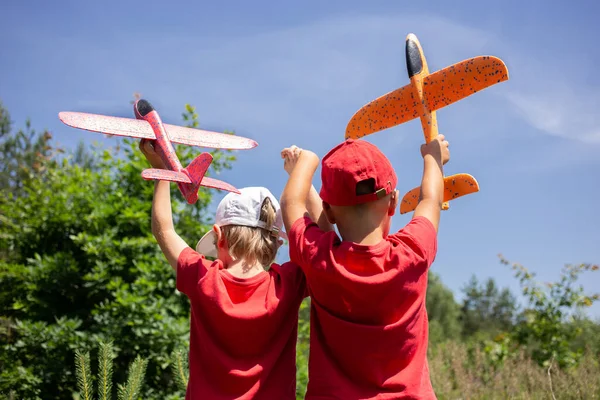赤いTシャツを着た2人の無名の男の子が 青い空におもちゃの飛行機を持って背を向けて立っています ゲーム 飛行機のパイロットになりたいという願望の概念 — ストック写真