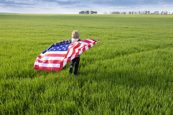 ndependence Day. National symbol of freedom and independence of the United States of America. child holds American flag behind back and runs through green meadow. Pride to be an American