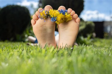Güneşli bir günde çocukların çıplak ayakları ve küçük çiçek çelenkleri yeşil çimlerin üzerinde uzanır. pozitif atmosfer, merhaba yaz, doğanın enerjisi, dikkatsizlik, mutlu çocukluk. Merhaba yaz. Rahatla, güneşlen.