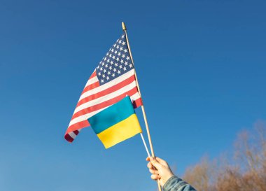 Amerikan bayrağı ve Ukrayna bayrağı mavi bulutsuz gökyüzüne karşı. İki ülke arasındaki işbirliği ve dostluk kavramı. Ukrayna 'nın Rusya ile savaşı kazanması için ABD' den yardım