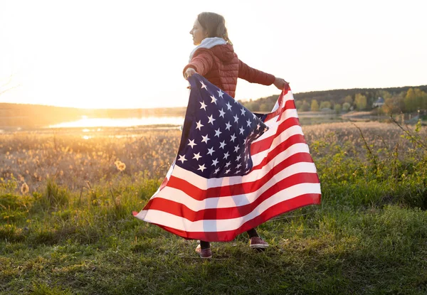 快乐的女孩漫不经心地站在夕阳西下 背着美国国旗 独立日 美利坚合众国自由和独立的国家象征 — 图库照片