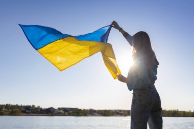 Kadın silueti, rüzgarda dalgalanan bir Ukrayna bayrağını tutuyor. Güneşle güzelce aydınlatılıyor. Ukraynalılar savaşa karşıdır. Ukrayna 'ya dikkat çekiyor. Savaşı durdurun.