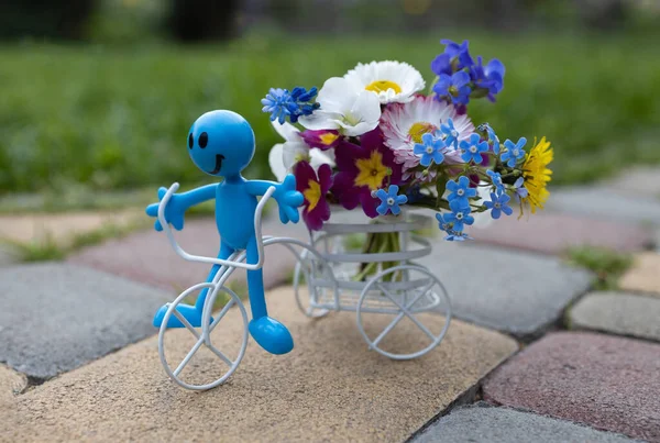 white souvenir bicycle with a bouquet of flowers in a basket and a miniature toy happy man. Birthday card, mother\'s day with love. atmosphere of love, positivity and joy. Flower delivery