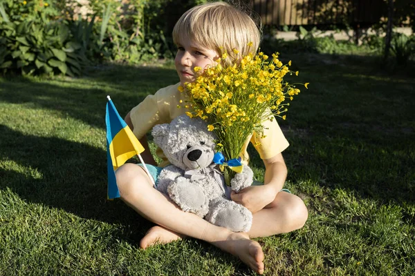 Несчастный Семилетний Мальчик Сидит Траве Плюшевым Мишкой Украинским Флагом Букетом — стоковое фото