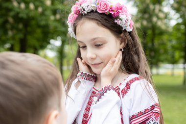 7 yaşındaki bir kızın yüzü, küçük kardeşinin elini tutuyor. Her iki çocuk da nakışlı Ukrayna giysileri giyiyor. Aile, birlik, savaş sırasında birbirinize iyi bakın ve destek olun. Bağımsızlık Günü.