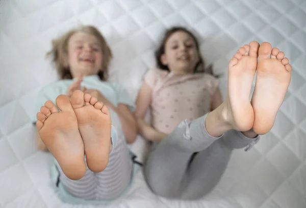Two children lying on the bed cheerfully raised their bare feet up. children's toes and heels. brother and sister friends have fun on parents big bed, family joy