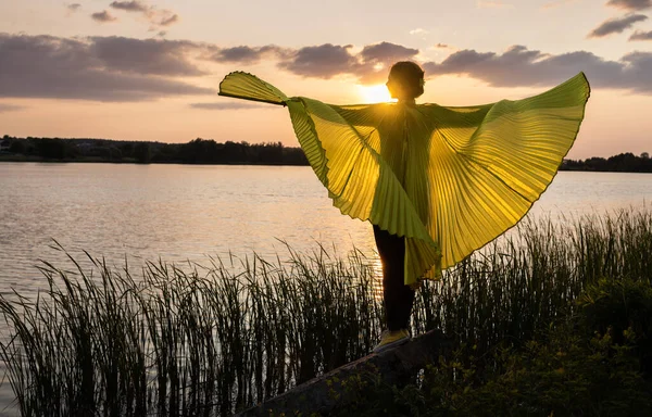 elegant woman stands at sunset spreading her wings. Sunset and silhouette, beauty of nature and human. Fantasies, dreams, aspirations for a brighter future