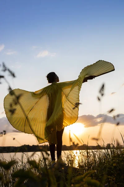 elegant female silhouette stands at sunset , spreading wings against sun. beauty of nature and human. Fantasies, dreams, aspirations for bright future, revival of Ukraine, yellow and blue colors