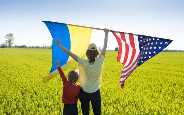 在阳光灿烂的日子里 背着孩子站在那里 升起两面巨大的国旗 美国国旗和乌克兰国旗 合作与友谊的概念 美国对乌克兰的援助赢得了对俄战争 — 图库照片
