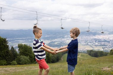 Yedi yaşındaki iki çocuk alçak dağların yamacında el ele tutuşuyorlar. Sağlıklı yaşam tarzı, hafta sonu yürüyüşü, destek ve arkadaşlık, aktif yaz tatili. Doğal manzara