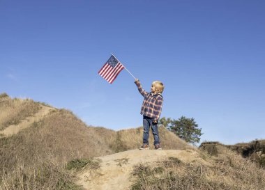 6 yaşındaki vatansever çocuk mavi gökyüzüne karşı gururla Amerikan bayrağını kaldırdı. Amerika Birleşik Devletleri Bağımsızlık Günü 'nü kutluyoruz. Mutluluk, başarı, özgürlük, ulusal sembol