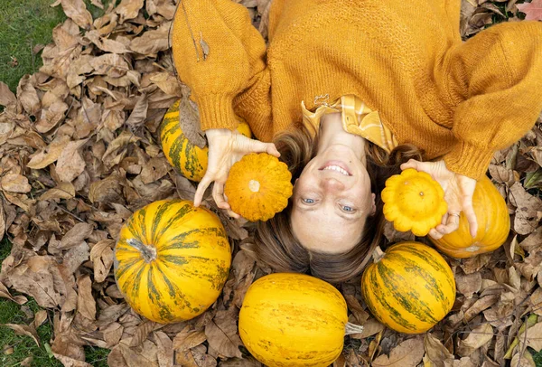 快乐的女人躺在明亮的黄橙色南瓜中间的干枯的树叶上 秋天的蔬菜收获 感恩节 万圣节的准备工作有选择的重点 从上面看 — 图库照片