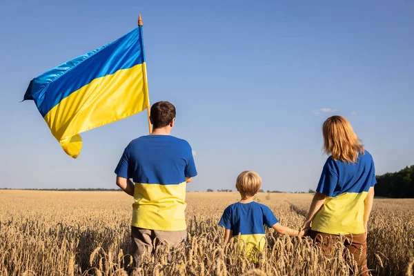 Ukrainian family in yellow-blue t-shirts and flag of Ukraine stands with their backs among ears of corn in wheat field. national self-awareness, love for homeland. faith in victory. Independence Day.