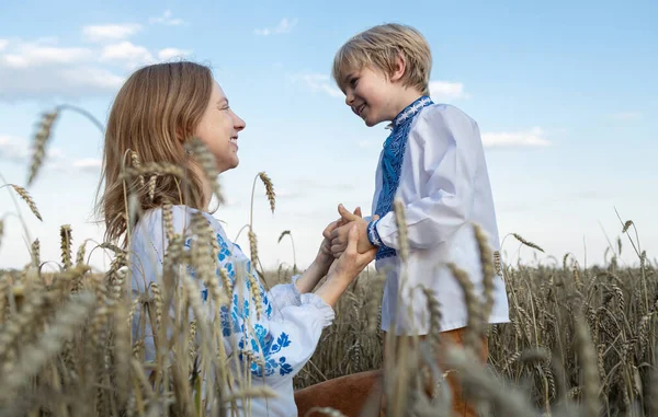 boy and woman, mother son in embroidered national clothes are sitting among spikelets in wheat field. Ukrainian family, refugees, unity, support, tenderness of motherhood. Stop war. stand with Ukraine
