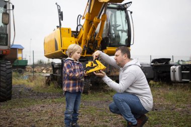 İnşaat malzemelerinin arka planındaki çocuk ve adam kazıcılar oyuncak buldozerleri hevesle inceliyorlar. Gününü oğlunla geçir. Çocuğun makinelere ve işlerine olan ilgisi. Babalar Günü.