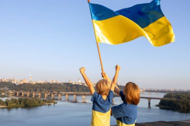 Anne ve oğlu, Kyiv 'deki Dnieper Nehri' nin ve gökyüzünün karşısında, evin çatısında dikiliyorlar. Vatanseverlik, Ukrayna 'daki savaşa dikkat çekmek. Ukrayna 'yı destekleyin. Bağımsızlık Günü. Zafere olan inanç. Savaşı durdurun.