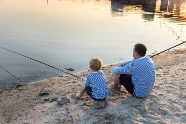 Dad and son are relaxing together, sitting on river bank with fishing rod. father\'s day concept. Family fun for weekend. joint hobby for parent and offspring. be like dad, educate patience