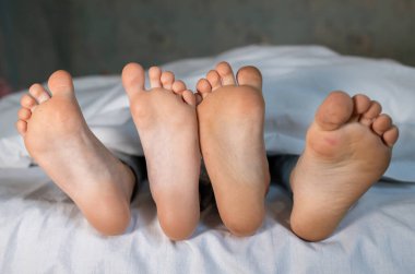 Yatakta aynı battaniyenin altında yan yana yatan iki çocuğun çıplak, temiz ayakları. Sabah rahatlaması, rahat dinlenme. Bebek ayaklarının şirin resimleri.
