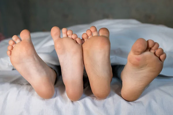 ベッドの上の同じ毛布の下に横たわっている 2人の子供の裸足のきれいな足 朝のリラックス 居心地の良い休息 赤ちゃんの足のキュートな写真 ストックフォト