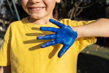 Sarı tişörtlü küçük okul çocuğu elini maviye boyayıp Ukrayna bayrağını oluşturuyor. Ukrayna 'nın Bağımsızlık Günü. Vatanseverlik kavramı. Ukrayna 'nın çocukları savaşa karşıdır.