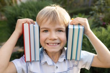 Sevimli, neşeli 7 yaşındaki çocuk, yüzünün yanında birkaç kitap tutuyor. Çocukken kitap okumak, meraklı çocuk, bilgi güçtür. Kitap günü. Okula dönmek, ilginç bir eğitim.