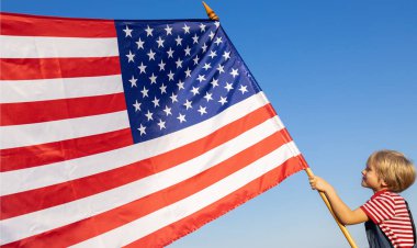 Çocuk gururla büyük bir Amerikan bayrağını tutuyor. Mavi gökyüzünün arka planında. Güneş ışığıyla aydınlatılıyor. Amerika Birleşik Devletleri 'nin Bağımsızlık Günü. Özgürlük, güven, ulusal sembol