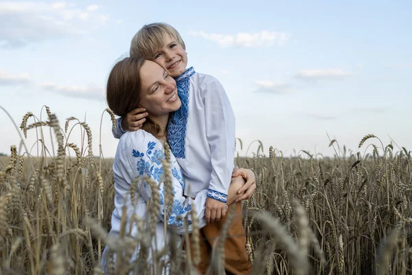 boy and a woman in embroidered shirts tenderly hug each other among the ears of corn in a wheat field. Ukrainian family, unity, support for Ukraine. Independence Day