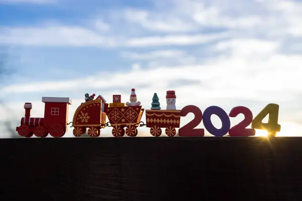 Happy New Year and Merry Christmas. children\'s wooden holiday train and numbers 2024 against the background of the sky and sun rays. festive mood. Time to make wishes, bright future