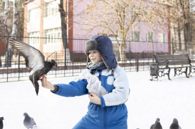 Sevimli anaokulu çocuğu kış günü elini uçan bir güvercine uzatıyor. Bir çocuk sokakta yürüyor ve kuşlarla ilgileniyor.