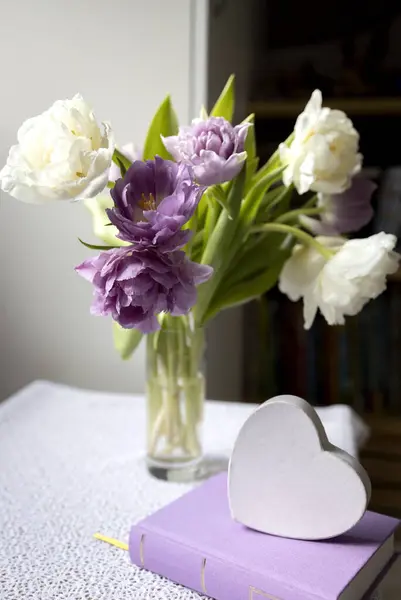 bouquet of tulips on the table near a book and a white heart. concept of loving reading, self-education, aesthetics, wisdom and knowledge. digital detox. book day