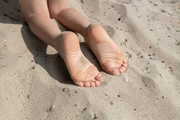 The child\'s bare feet lie on the warm sand. Carefree childhood, the joy of summer. holidays and healthy lifestyle concept. Healthy feet, lovely toes.