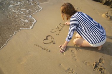 Çizgili deniz kıyafetleri içinde tanınmayan bir kadın deniz kıyısında otururken kuma 