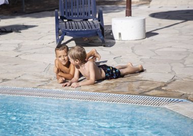 İki çocuk, 6 yaşında çocuklar, havuz kenarında yüzüyorlar ve güneşli bir günde güneşleniyorlar. İyi bir ruh hali, yaz tatili, arkadaşlık, ilginç bir çocukluk. Sıcak hava