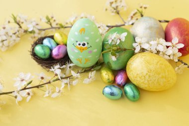 Küçük bir yuvada Paskalya renkli yumurtalar ve renkli yumurtalar parlak sarı bir zemin üzerinde beyaz çiçekli dallar. yumuşak, parlak Paskalya kartı. dini bayram