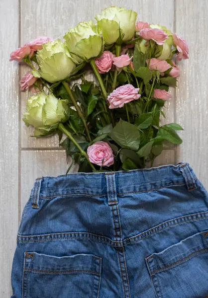 Jeans and a bouquet of pink and green roses. Mother\'s Day, Valentine\'s Day. Flower surprise with love