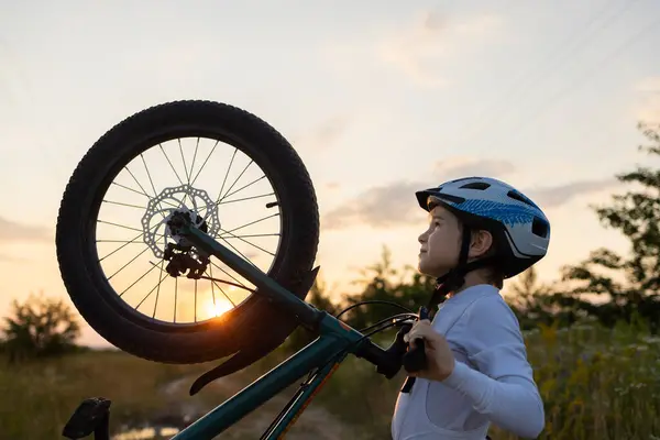 face of a boy in a bicycle helmet with a bicycle against the backdrop of the sunset sky and sun. The silhouette of a bicycle wheel and the profile of a child. Healthy lifestyle, sports recreation
