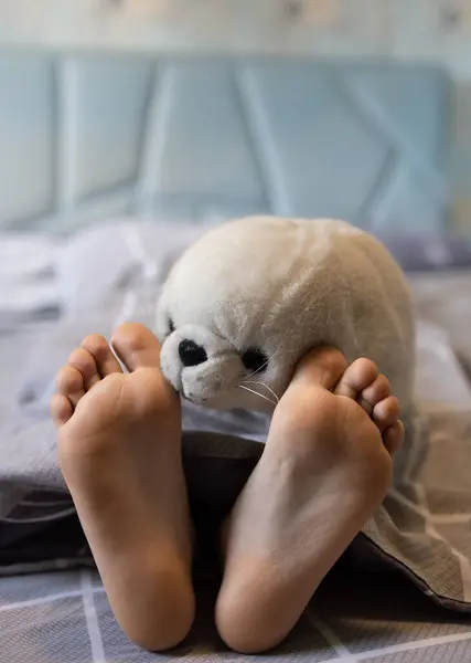 baby's bare feet on the bed close-up and a soft fluffy toy seal face. Good morning. A cozy sleeping place, sleep with pleasure in the company of your favorite toy, play at home on the bed