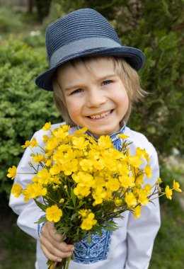 6-7 yaşlarında, geleneksel işlemeli gömlek, şapka ve bir buket düğün çiçeği takmış sevimli, neşeli bir Ukraynalı çocuğun portresi. Barış için çocuklar. Savaşı durdurun. Ukraynalı olmaktan gurur duyuyorum. Anneler Günü