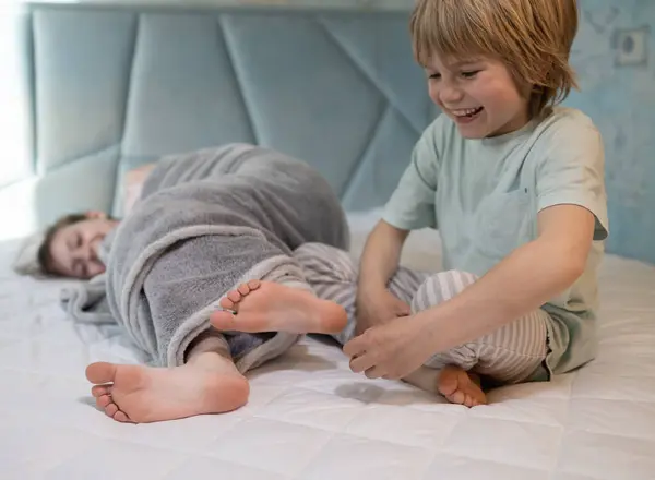 パジャマのかわいい子供たちは 自宅のベッドで遊んでいます 兄は妹の裸足をくすぐった 子供の陽気な子供時代 家で甘やかされ 居心地の良い休息 選択的な焦点 ストック写真