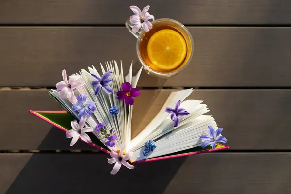 book standing vertically and small spring flowers between the pages, cup of tea on table, illuminated by sun. Picture of peaceful morning. atmosphere of relaxation, tea time. Read book with pleasure