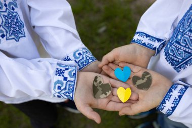 Askeri kamuflaj kumaşı ve sarı-mavi kağıttan kesilen dört kalp Ukrayna işlemeli gömlekli iki çocuğun avucunda yatıyor. Ukrayna 'daki savaşı durdurun. Silahlı Kuvvetler askerlerine sevgilerimle.