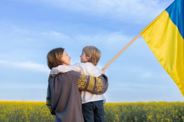 Ukraynalı aile, anne ve oğul. Çiçek açan bir ırz tohumu tarlasında mavi ve sarı bir bayrak taşıyorlar. Ukrayna 'nın Bağımsızlık Günü. Rusya ile karşılaşmada Ukrayna 'yı desteklemek. Savaşı durdurun.