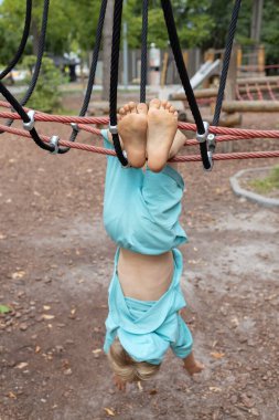 Sahada baş aşağı asılı çıplak ayaklı bir çocuk. Mutlu çocukluk kavramı. Çocuklar için eğlence. Şımart ve spor yap
