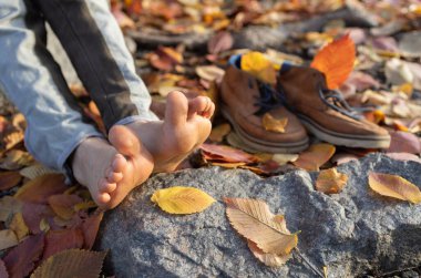 Kahverengi ayakkabıların yanında düşen yaprakların arasında bir çocuğun çıplak ayakları. Tasasız çocukluk, özgürlük, rahatlama, yürüyüş ve ılık sonbaharın tadını çıkarma. Aktif yaşam tarzı, Hint yazı.
