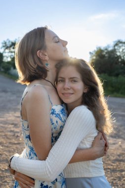 40 yaşını geçmiş mutlu bir anne ve arka plan ışıklarında şefkatle sarılan yetişkin kızı. Farklı kuşaklardan bir aile gittikçe yakınlaşıyor. Destek ve sevgi. Anneler Günü. Kızların Günü