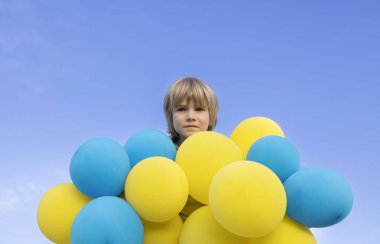 Güneşli bir günde gökyüzüne karşı bir sürü sarı ve mavi balonun arkasında endişeli bir çocuğun üzgün yüzü. Ukrayna ve Ukraynalı çocuklar için bir barış dileği. Savaşı durdurun.