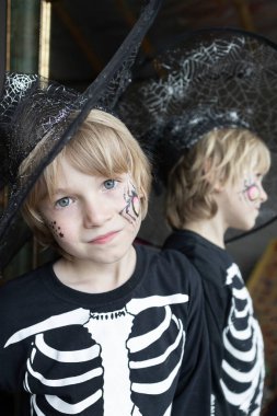 İskelet kostümlü ve siyah şapkalı bir çocuk aynanın yanında duruyor. Cadılar Bayramı kutlaması. Şeker mi şaka mı? Tatil için gizemli, şenlikli bir cadı imajı.