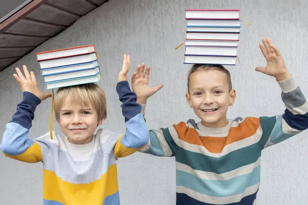 stock image Two brothers or friends for 7 years balance stacks of books on their heads. joyful meeting of classmates, back to school. Book Day. concept of reading, education, knowledge. Digital detox