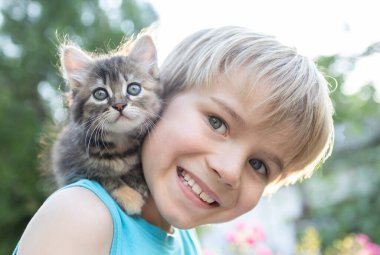 Neşeli çocuk güzel bir kediciği omzunda tutuyor. Kedi günü. Mutlu bir çocukluk. Kedi günü. Evcil hayvanla ilgilenmek