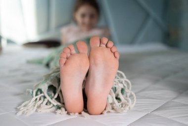 Yatakta battaniyenin altında yatan bir çocuğun çıplak ayaklarına odaklan. İyi sabahlar. İyi geceler. Rahat bir çocukluk, keyifle uyku, çocuksu şefkat, sağlıklı ayaklar.